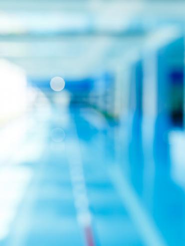 Unscharfes Bild eines modernen Schwimmbeckens mit blauer Wasseroberfläche und hellem, lichtdurchflutetem Raum.