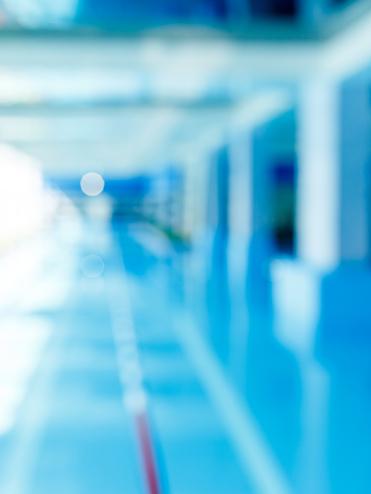 Unscharfes Bild eines modernen Schwimmbeckens mit blauer Wasseroberfläche und hellem, lichtdurchflutetem Raum.