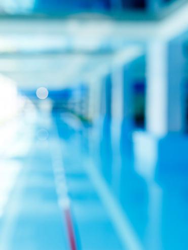 Unscharfes Bild eines modernen Schwimmbeckens mit blauer Wasseroberfläche und hellem, lichtdurchflutetem Raum.