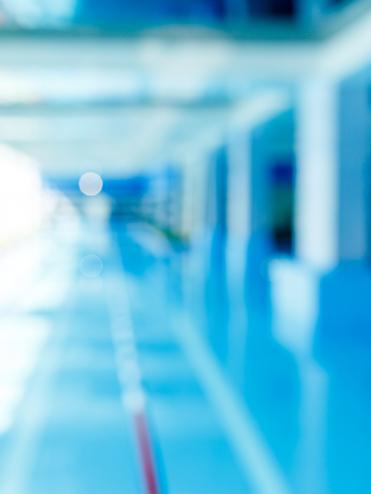 Unscharfes Bild eines modernen Schwimmbeckens mit blauer Wasseroberfläche und hellem, lichtdurchflutetem Raum.