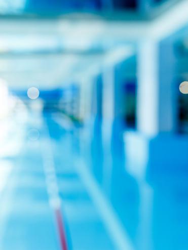 Unscharfes Bild eines modernen Schwimmbeckens mit blauer Wasseroberfläche und hellem, lichtdurchflutetem Raum.