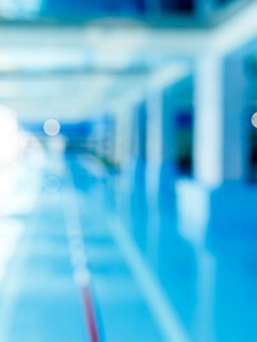 Unscharfes Bild eines modernen Schwimmbeckens mit blauer Wasseroberfläche und hellem, lichtdurchflutetem Raum.